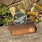 Photo of a silver sobriety coin with "15 YEARS" text, moon and sun design, displayed on a wooden stand with dried botanicals