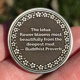 Photo of silver sobriety coin held in hand with Buddhist proverb text and flower border design