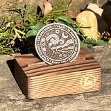 Photo of silver sobriety coin with Starry Night design displayed on wooden stand surrounded by greenery