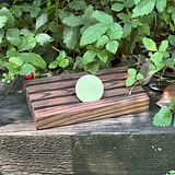Photo of pale green sobriety coin displayed on striped wooden stand outdoors