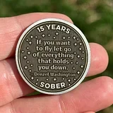 Photo of a silver sobriety coin held in hand, engraved with "15 YEARS" at top, a soaring hawk design, motivational quote, "SOBER" at bottom, and outdoor back...